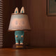 The Giant Sculptures Hidden Lamp Labubu Sculpture - 100cm is a blue bunny-inspired lamp with a lampshade over its head, ideal for modern interiors and perfect for adding charm to any warmly lit room.