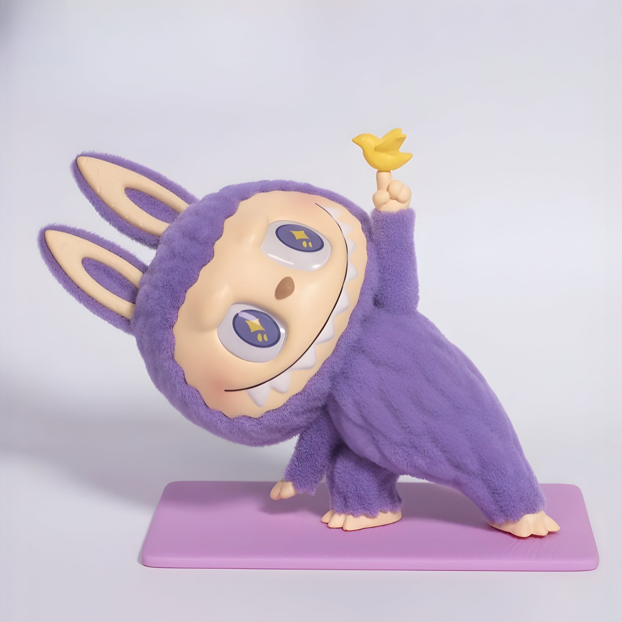 The Lazy Yoga Little Bird Labubu Sculpture - 100cm by Giant Sculptures features a charming, wide-eyed figure leaning on a lilac mat, smiling and holding a yellow bird aloft—an adorable fibreglass piece full of contemporary character.
