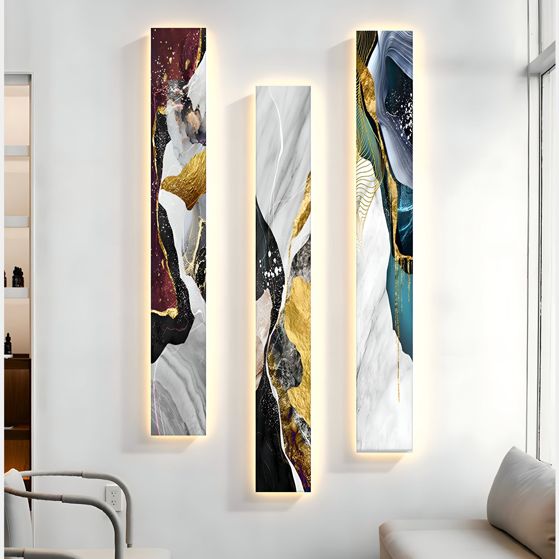 Three vertical pieces of the Floren Crimson Burst Canvas LED Wall Art by Giant Sculptures hang on a white wall, featuring gold, white, black, burgundy, and teal accents with intricate textures and swirls. A modern white chair is partially visible in front.