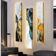 Three vertical panels of the Floren Oceanic Drift Canvas LED Wall Art by Giant Sculptures hang on the wall, featuring flowing designs in white, gold, black, teal, and orange. The art casts a warm glow onto a modern sofa and floor lamp for a contemporary living room setting.