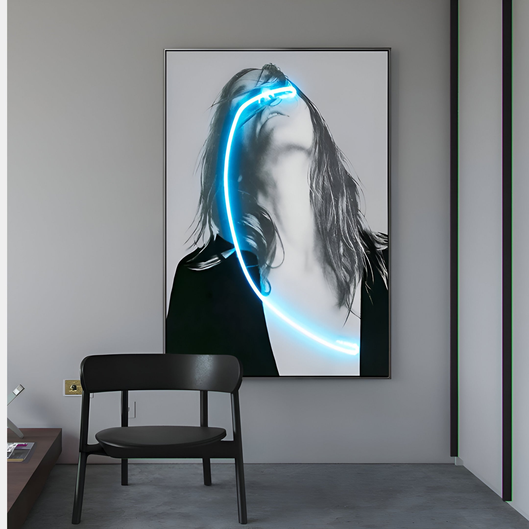 The Elysian Veiled Grace 3D LED Wall Art by Giant Sculptures features a framed black-and-white photo of a long-haired person, elegantly illuminated with a striking neon blue curve. It adorns a gray wall next to a black chair and wooden surface, exuding contemporary aesthetics.