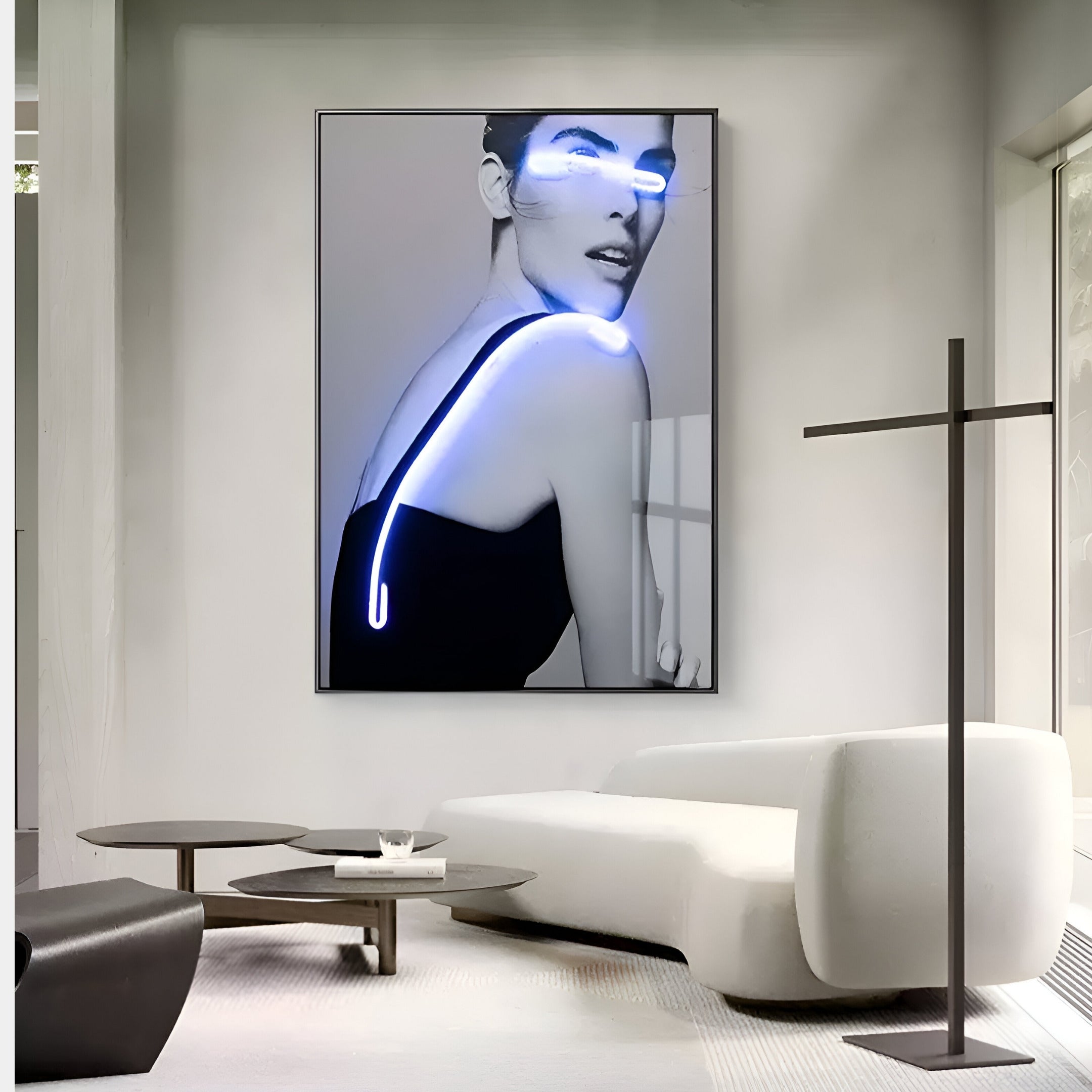 A modern living room highlights the Elysian Luminescent Gaze 3D LED Wall Art by Giant Sculptures, alongside a large black-and-white portrait of a woman with blue neon accents. A white curved sofa and round coffee table add minimalistic charm, with natural light streaming through a large window to enhance the aesthetics.