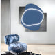 In a modern room, a blue, fluffy chair rests on a wooden floor. The wall features Giant Sculptures Gleam Azure Elegance 3D Leather LED Wall Art with a blue shape outlined in light against a dark gray rectangle. The ambiance is contemporary and stylish.