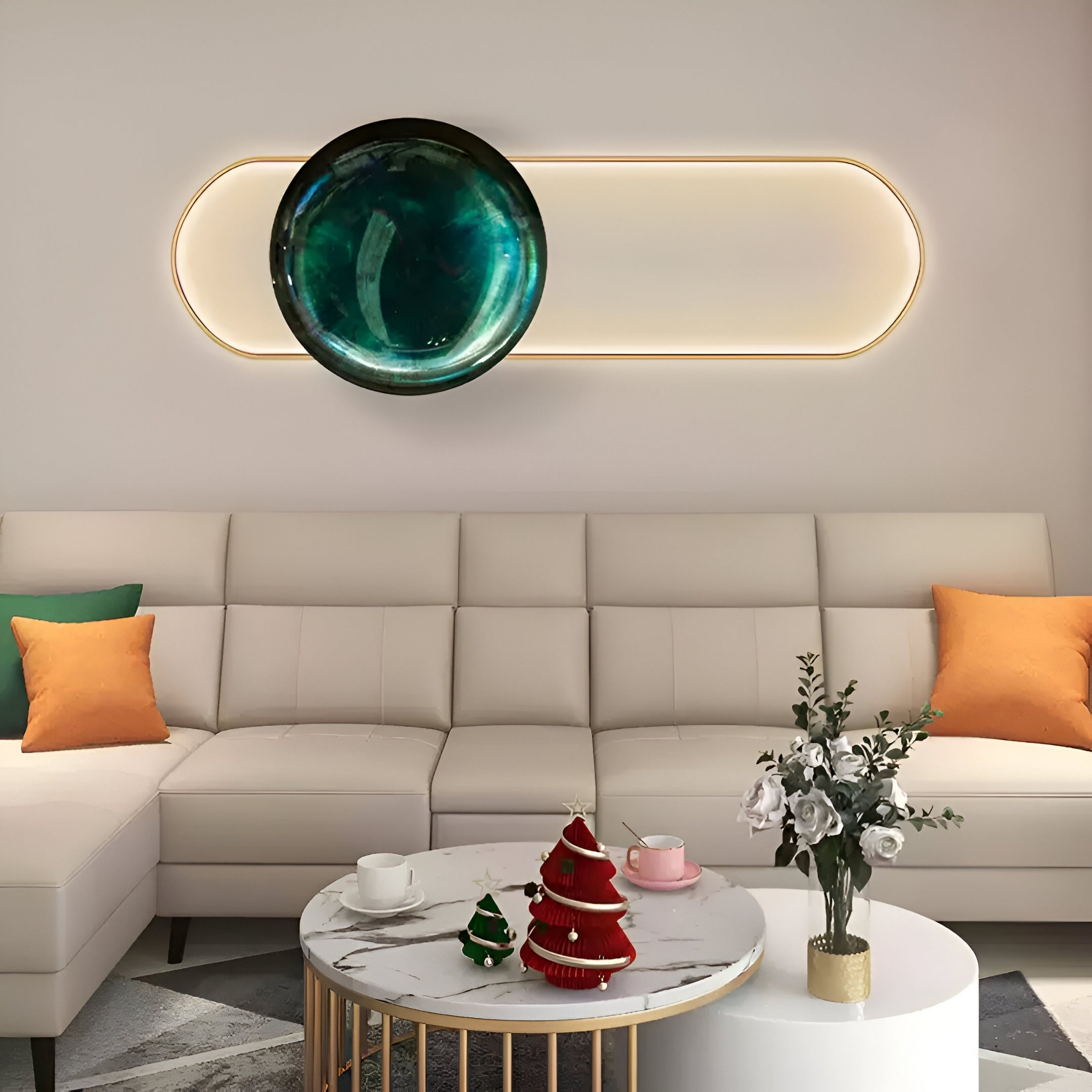 A modern living room showcases a white sectional sofa with green and orange pillows, accented by a marble coffee table holding red and green cone-shaped objects and a vase of flowers. The space is elegantly enhanced by Giant Sculptures Vitreon Emerald Flat Crystal Porcelain With Gold Frame Wall Art.