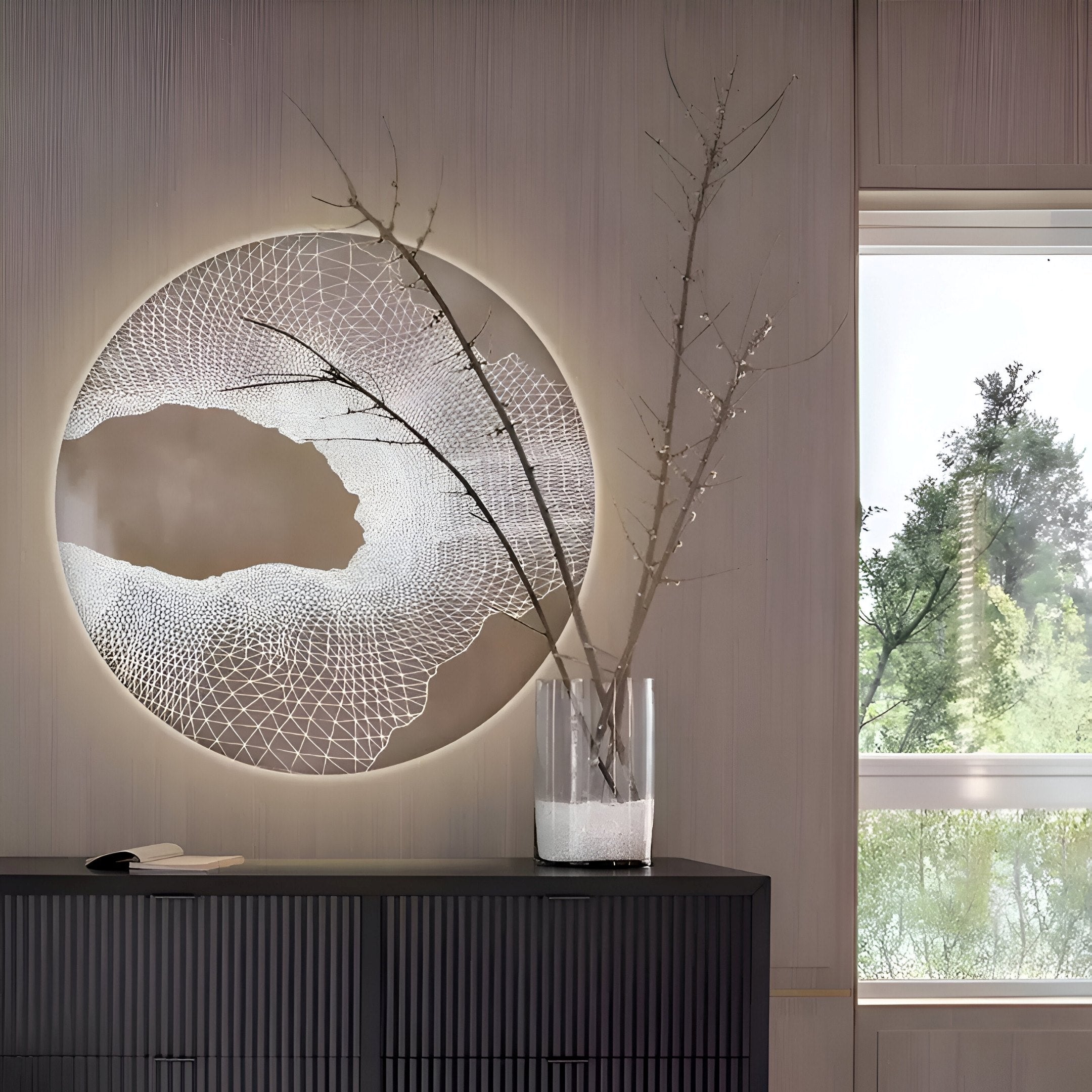 The Earthlight Amber Glow 3D Textured Oil Painting LED Wall Art from Giant Sculptures, featuring intricate lattice designs in amber tones, is displayed above a dark console table. A glass vase with bare branches adorns the table while natural light illuminates the minimalist interior.