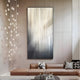 A modern living room features a tan leather sofa with gray and white pillows. The ambiance is enhanced by the Giant Sculptures Celeste Lightfall LED Wall Art featuring vertical lines, while pendant lights cascade from the ceiling, adding elegance to this contemporary space.