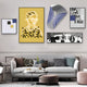 A modern living room with a gray sofa and patterned cushions exhibits abstract aesthetics. The wall features Orison Geometric Play Crystal Porcelain 3D Wall Art by Giant Sculptures, alongside a yellow portrait and black and white photo. A small table holds decor items and plants.