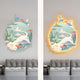 The Gaia Soft Sage Wood Engraving 3D LED Wall Art by Giant Sculptures depicts a stylized mythical creature with tree and mushroom elements. The left piece is in pastel colors, while the right one features an LED yellow outline, both elegantly situated above gray sofas.