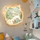 A cozy room features the Gaia Misty Pastel Wood Engraving 3D LED Wall Art from Giant Sculptures, depicting peaceful nature with birds and a deer. A child painted on the wall enjoys ice cream. Shelves of toys, books, baseball caps, plus a lamp and chair in the corner add charm.