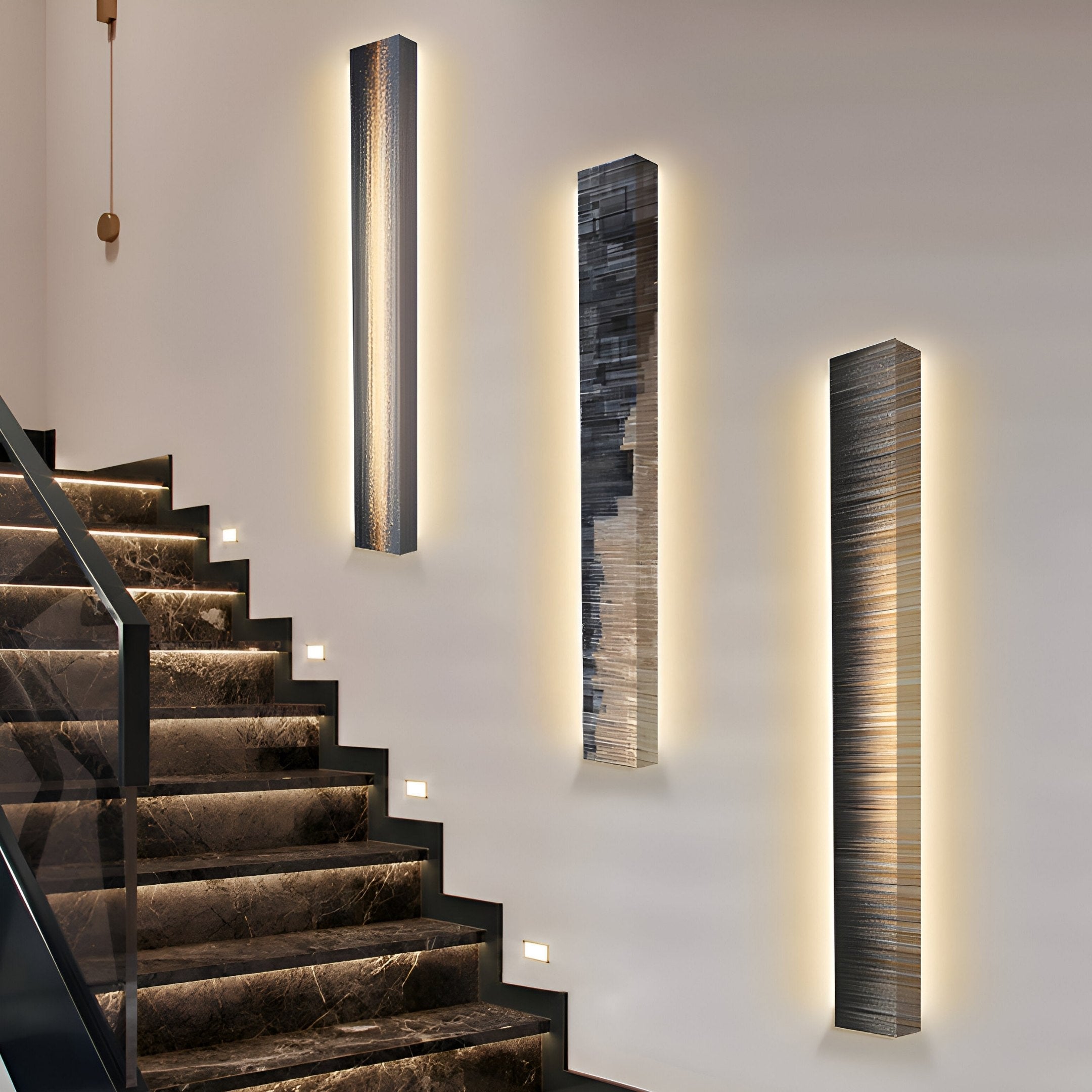 The modern staircase with dark marble steps is enhanced by sleek, rectangular wall lights featuring a metallic textured finish with subtly glowing edges, reminiscent of the Radiance Amber Dusk Canvas LED Wall Art by Giant Sculptures, adding an artistic touch to the minimalistic and elegant setting.