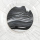 The Ventus Onyx Strata Wood Carving by Giant Sculptures showcases black and white swirling patterns, reminiscent of onyx strata. Surrounded by a textured white circular border, it creates an impressive 3D LED wall art effect.