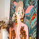 The Solana Bohemian Muse Wood Relief 3D LED Wall Art by Giant Sculptures features stylized art of a figure adorned in pink with tiger designs and large earrings, set against a bold botanical backdrop with vibrant leaves and flowers. Painted blue tears add an artistic flair to the facial features.