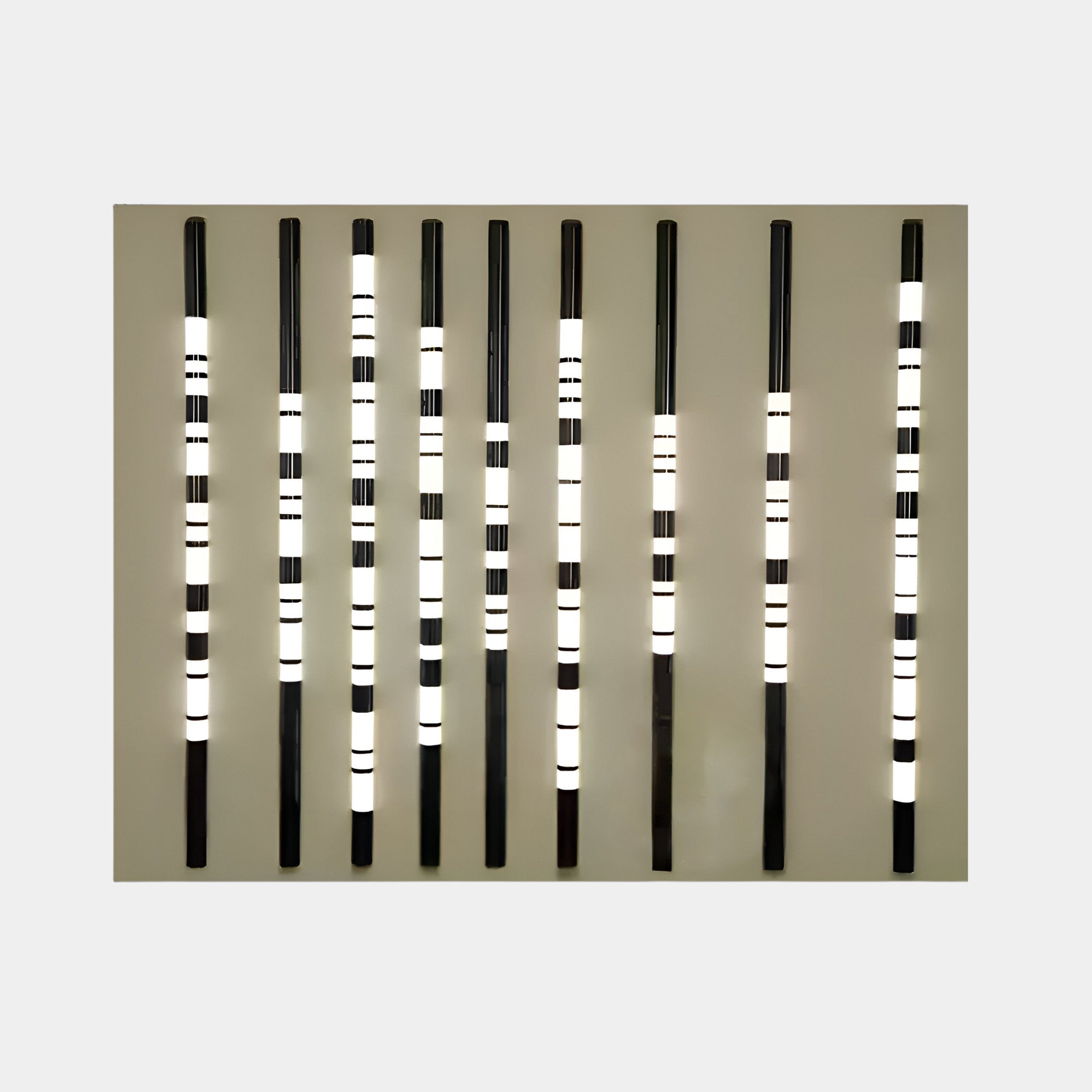 The Strata Slate LED Wall Art by Giant Sculptures features nine vertical black rods with glowing white lights set against a plain slate-gray wall, forming a contemporary barcode pattern that creates a striking visual effect.