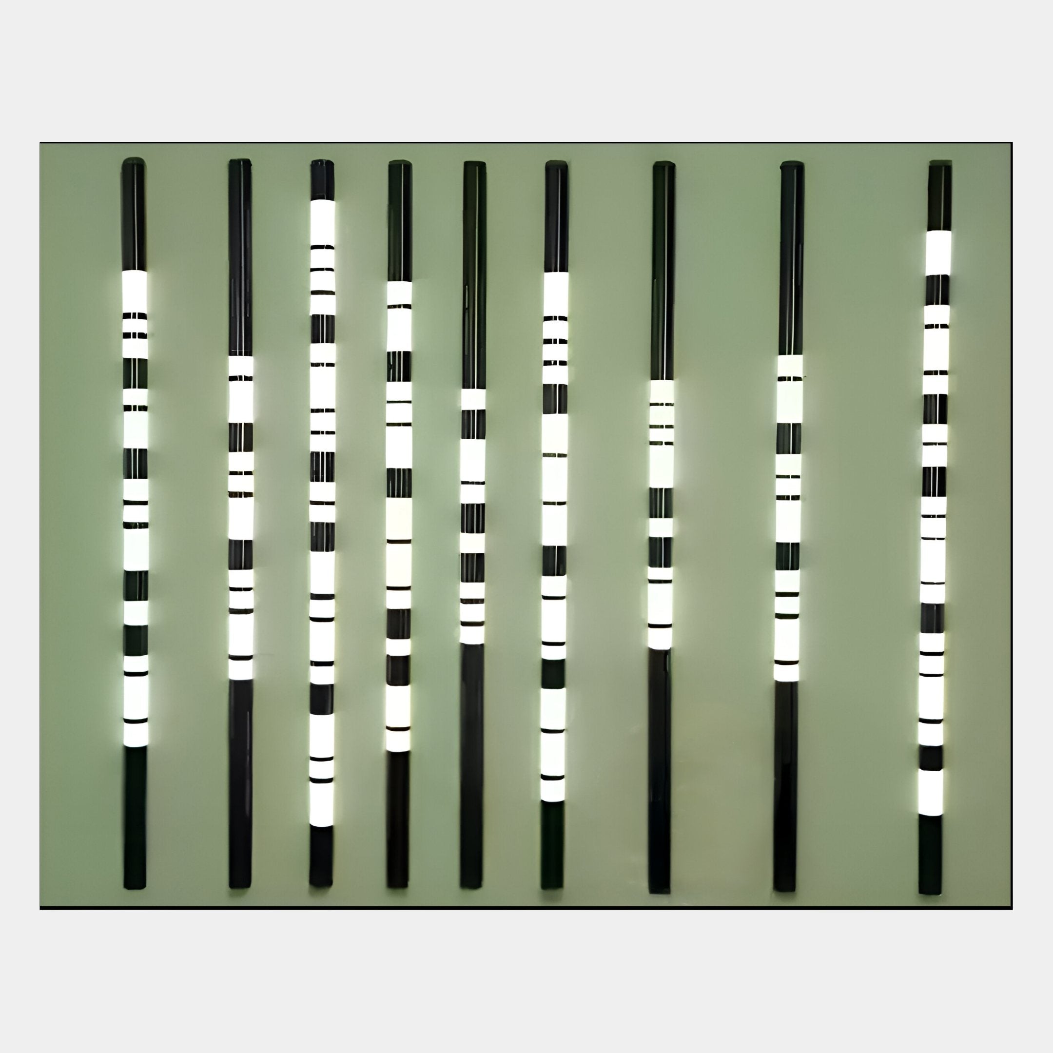 The Strata Olive LED Wall Art by Giant Sculptures features nine vertical black rods with glowing white bands on an olive background, adding a modern aesthetic to any space.