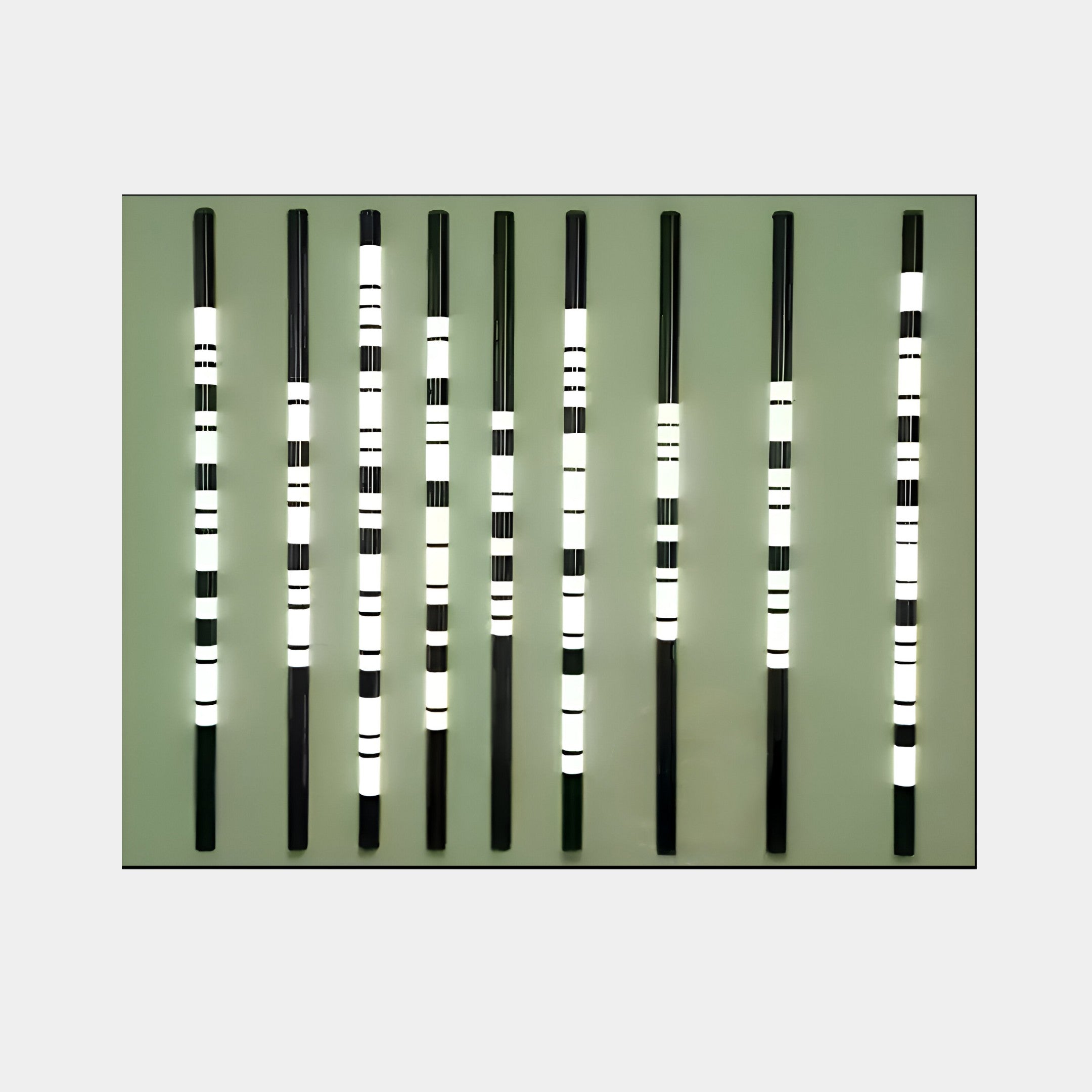 Strata Olive LED Wall Art by Giant Sculptures features nine vertical black rods with white and black bands on a muted green background, creating a rhythmic and modern aesthetic for contemporary interiors.