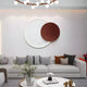 A contemporary living room showcases a white sofa with patterned and solid cushions. The Soluna Copper Acrylic 3D LED Wall Art by Giant Sculptures adds visual intrigue above, while a round coffee table with books and a plant rests on a patterned rug, illuminated by an integrated LED tube light.