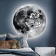 A bedroom boasts a large, glowing moon mural and is enhanced by the Cosmos Astronaut Adventure UV Wood Carving LED Wall Art from Giant Sculptures, depicting an astronaut with moon balloons. The bed has plush toys and white-blue bedding, complemented by a sleek white nightstand.