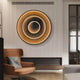 In a modern living room, the Reflex Gold Mirror 3D LED Wall Art from Giant Sculptures showcases stunning concentric rings. An armchair with a light blue pillow rests on wooden flooring. The ribbed-textured wall enhances the luxury decor, while glass panels to the right add elegance.