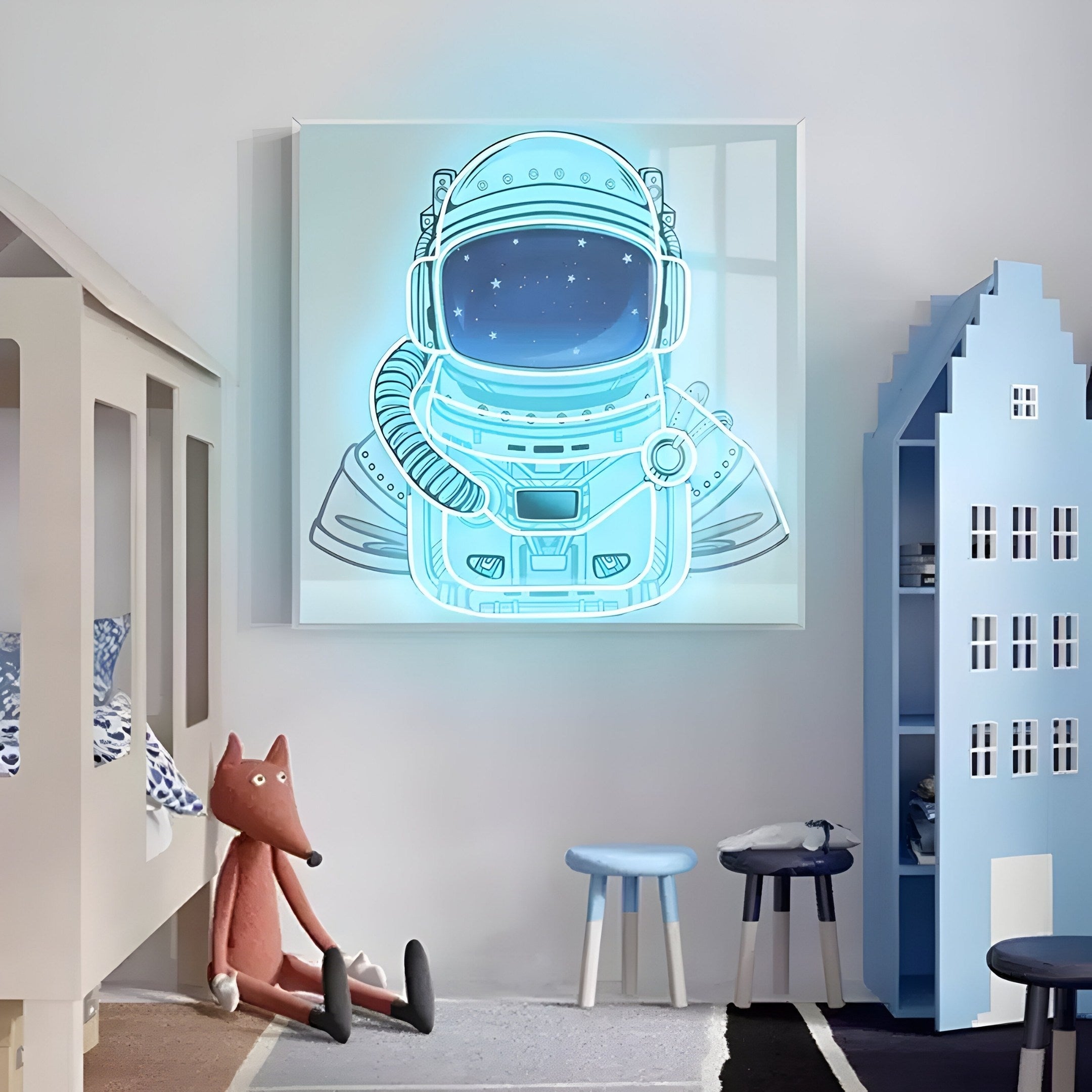 A childrens room with white walls features the Giant Sculptures Stellar Neon Aqua Acrylic 3D LED Wall Art of an astronaut suit. A fox plush toy rests near a bed, and a blue house-shaped cabinet. Two blue stools are positioned in front of the vibrant artwork.