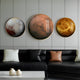 A modern living room showcases a black leather sofa with light cushions. Above, three Galaxia Mars Crystal Porcelain LED Wall Art pieces by Giant Sculptures resemble planets against the gray wall. Two small white vases on a low table add subtle elegance to this cosmic scene.