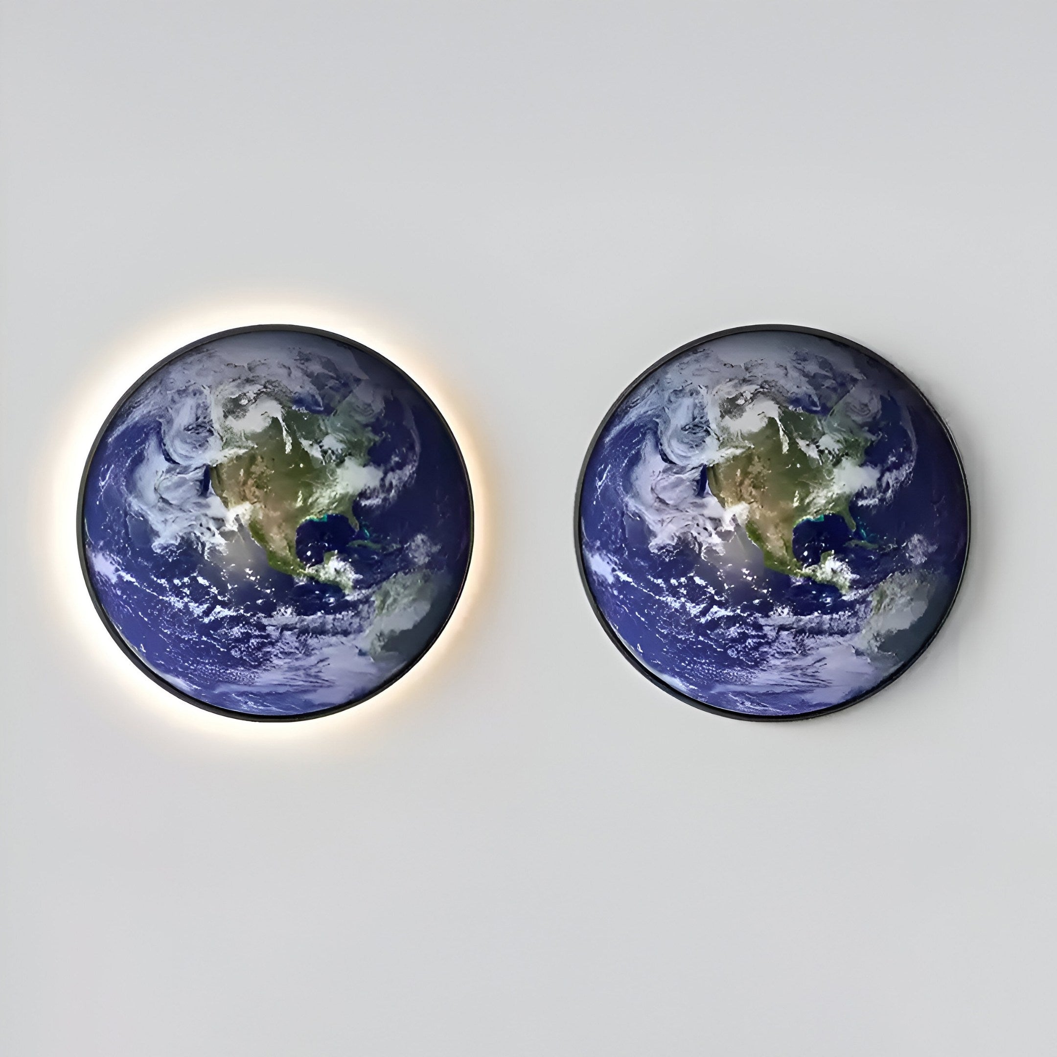 The Galaxia Earth Crystal Porcelain LED Wall Art by Giant Sculptures features two spherical Earth-like objects with North America visible. The left sphere emits a glowing halo, while the right is unlit, both encased in brushed aluminum.