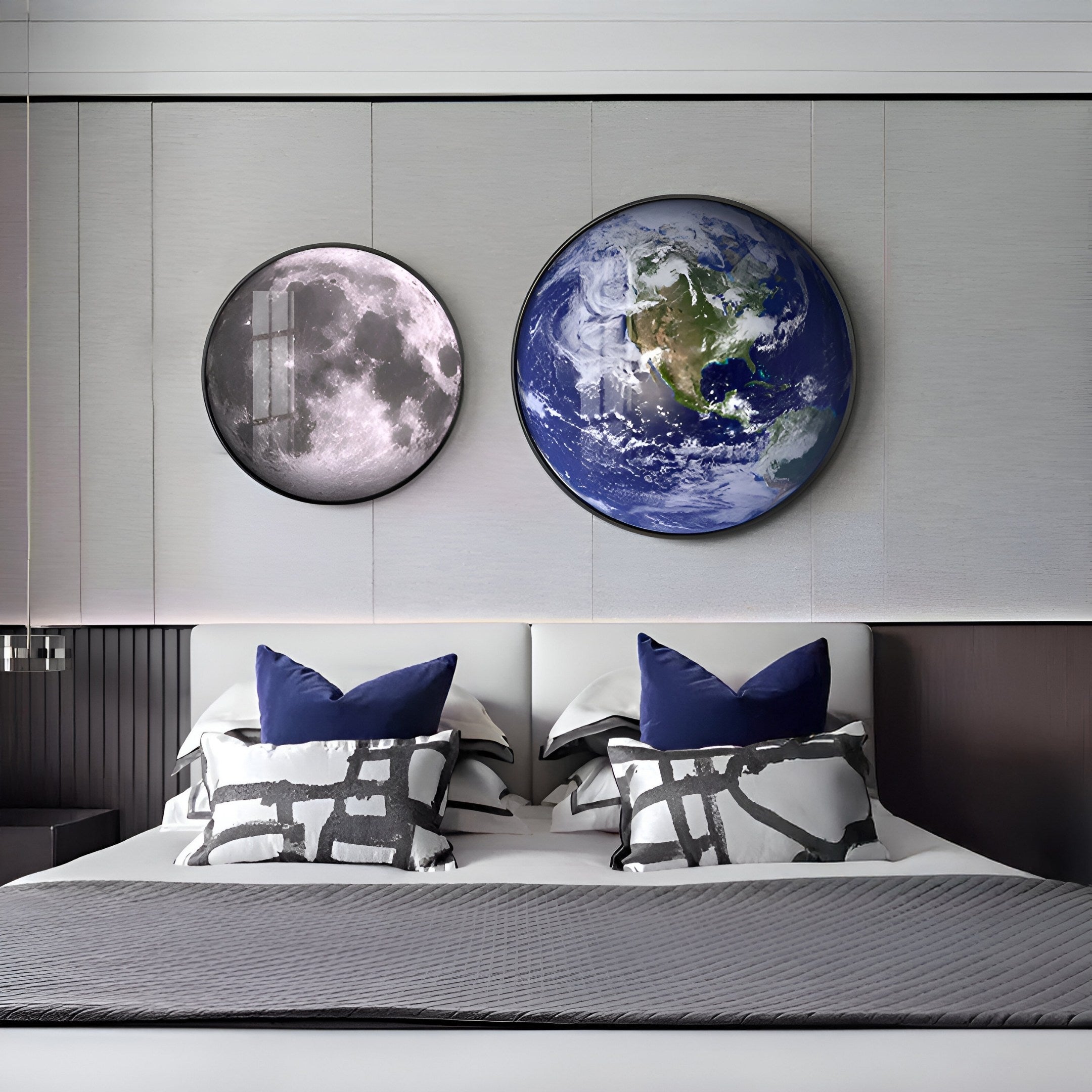 A modern bedroom is styled with a bed featuring white and gray bedding, three patterned pillows, and blue ones behind. Above it hangs the Galaxia Moon Crystal Porcelain LED Wall Art by Giant Sculptures, depicting the moon and Earth from space for a lunar-themed touch.