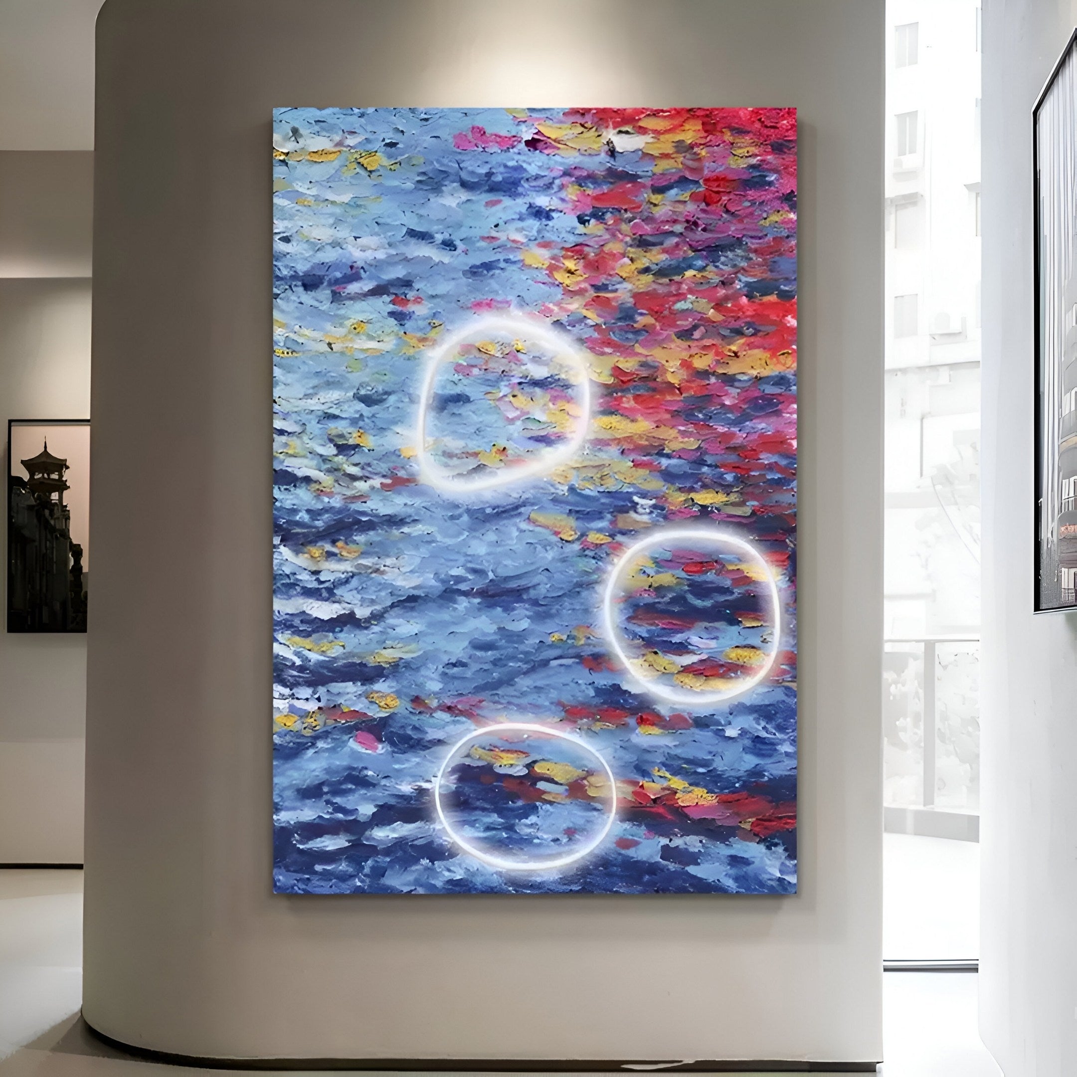 The Elysian Ocean Ember Oil Painting 3D LED Wall Art by Giant Sculptures is a large abstract piece with textured, vibrant pigments in red, blue, yellow, and white. It features three circular neon lights on the canvas, creating stunning 3D art displayed in a modern gallery space.