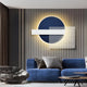 A modern living room features the Aeon Midnight Indigo Leather 3D LED Wall Art by Giant Sculptures. Against the wall, an indigo leather sofa sits with gray and black cushions. Nearby is a round, gray lounge chair, all set on a textured gray backdrop with warm lighting enhancing its contemporary look.