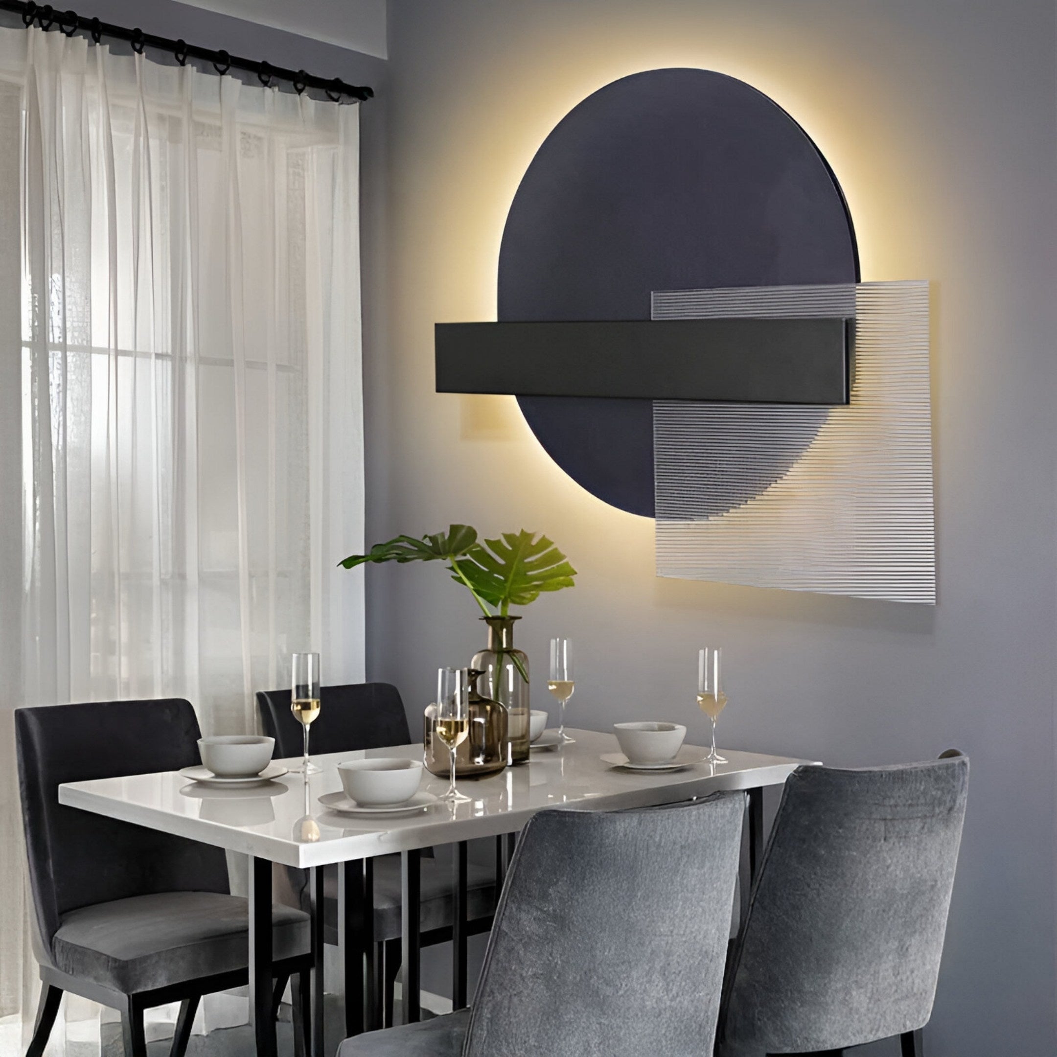 A modern dining area features a white table set for four with plates, bowls, wine glasses, and a green leaf centerpiece in a vase. Gray chairs surround the table, while the wall boasts the Aeon Onyx Graphite Leather 3D LED Wall Art by Giant Sculptures with circular and rectangular elements.