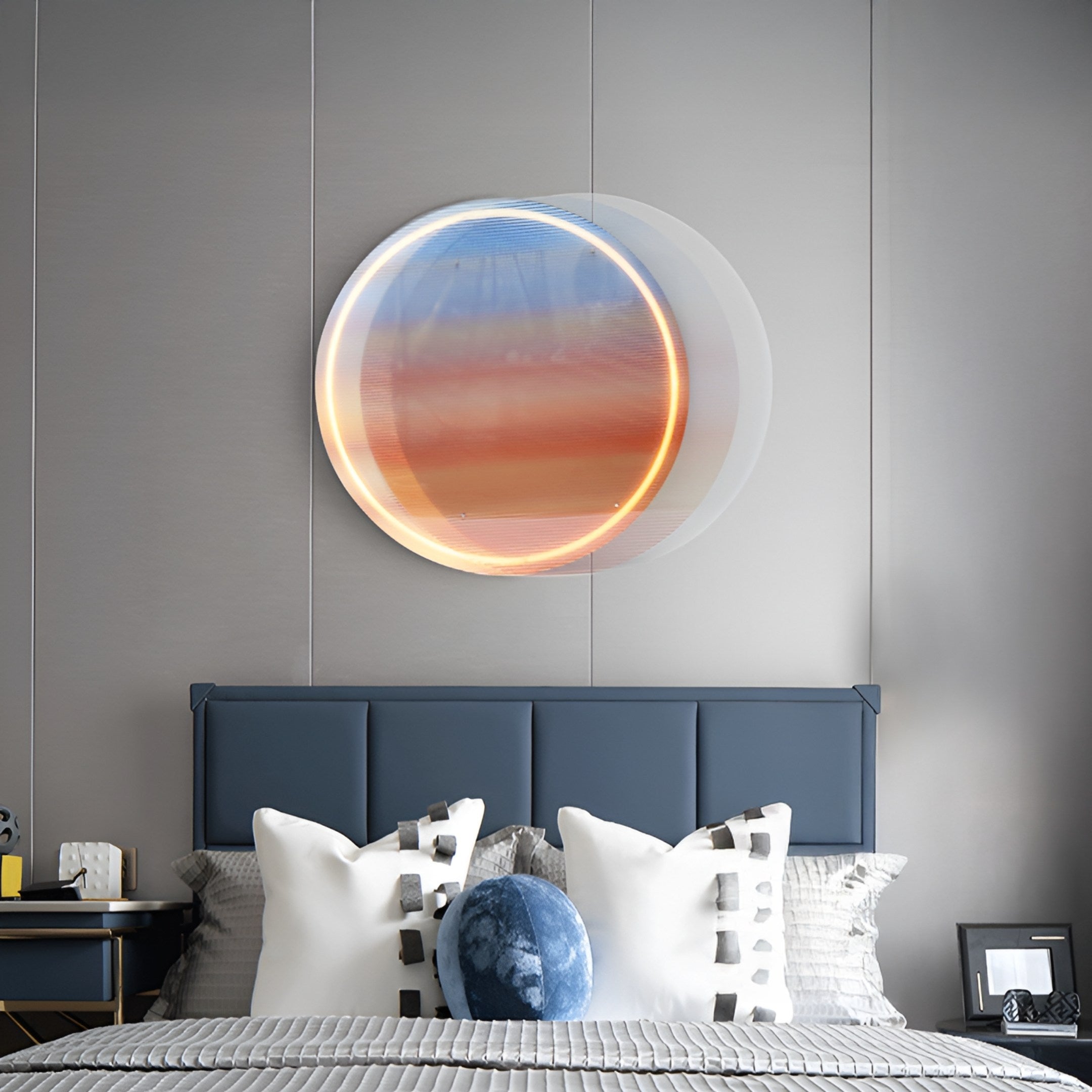 A modern bedroom features Giant Sculptures Chromia Sunrise Glow Acrylic LED Wall Art above a bed with a dark blue headboard. The art displays a layered gradient of blue, orange, and cream. Two white pillows and a blue round cushion add charm to the bed.