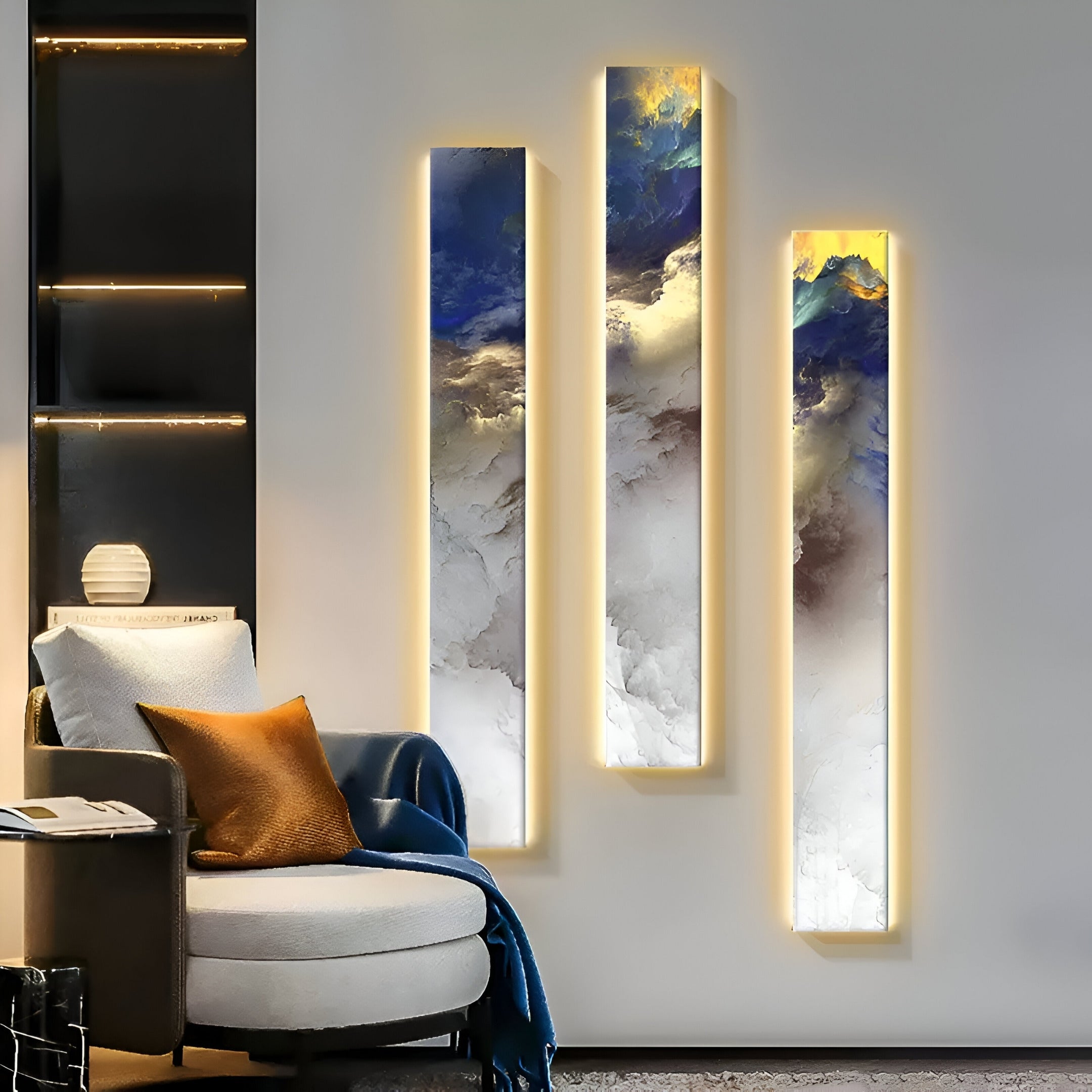 A modern living room features a cozy chair with an orange pillow and Chroma Blue Cloudlike Gradients blanket. Three vertical abstract paintings enhance the ambiance, while Giant Sculptures LED Wall Art Canvas on a small shelf to the left adds sophistication.