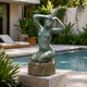 Large Contemporary Kneeling Female Figure Bronze Sculpture by Giant Sculptures with verdigris patina on a stump base, displayed on a stone plinth beside a poolside garden.