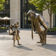 Large Contemporary Rotund Man and Defiant Girl Bronze Sculpture by Giant Sculptures, 200cm, shown on a paved plaza outside a café and modern building.