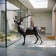 Large Traditional Bugling Bull Elk Bronze Sculpture by Giant Sculptures displayed in a modern glass-walled hallway beside a courtyard garden.