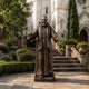 Large Traditional Robed Blessing Figure Bronze Statue by Giant Sculptures, 220cm friar with arms outstretched, displayed on a stone courtyard beside a church.