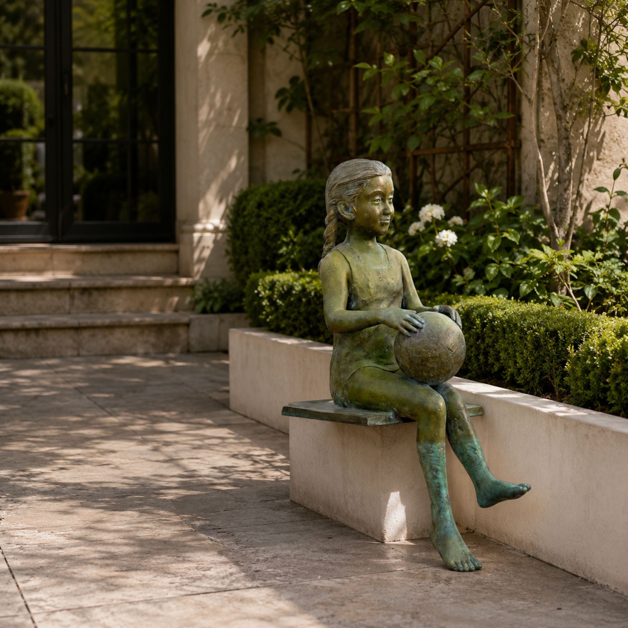 Large Traditional Seated Girl Bronze Sculpture, 130cm, green-patina bronze girl with braided hair holding a ball, seated on a garden ledge amid hedges.