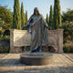 Life-Size Classical Jesus Christ Bronze Statue, 300cm, arms outstretched on a round pedestal, garden setting with stone bench and cypress trees.