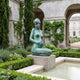 Life-Size Classical Kneeling Female Figure Bronze Sculpture by Giant Sculptures in verdigris patina, displayed on a stone plinth beside a garden pool and arches.