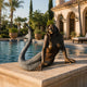 Life-Size Classical Reclining Mermaid Bronze Sculpture by Giant Sculptures on a travertine pool edge, two-tone brown torso and silver scaled tail curving upward.