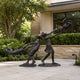 Life-Size Contemporary Children Playing Bronze Sculpture, 200cm, showing two figures swinging a third child through the air, set on a stone patio near greenery.