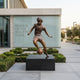 Life-Size Contemporary Footballer Dribbling Bronze Sculpture by Giant Sculptures on a black plinth outside a modern Museum of the Beautiful Game entrance.