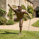Life-Size Contemporary Golfer Bronze Sculpture by Giant Sculptures on a lawn, mid follow-through with raised fist and club resting on turf beside a stone house.