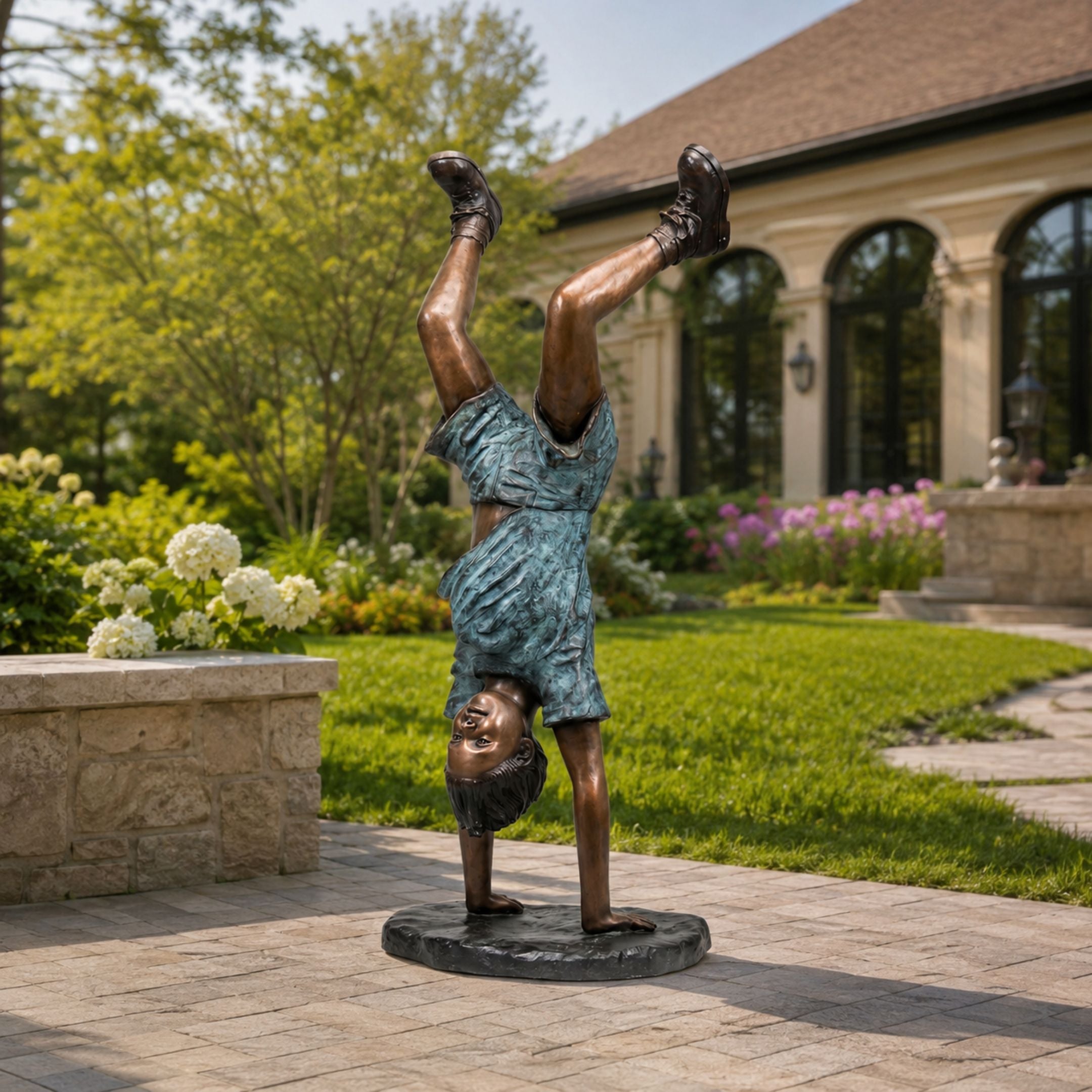 Life-Size Contemporary Handstand Child Bronze Sculpture, 130cm, on a garden patio with lawn, flowers, and a house facade in the background.