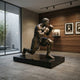 Life-Size Contemporary Kneeling Boxer Bronze Sculpture by Giant Sculptures in warm brown patina, displayed on a black plinth in a wood-paneled gallery room.