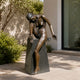 Life-Size Contemporary Seated Female Figure Bronze Sculpture by Giant Sculptures on a dark granite trapezoidal plinth in a sunlit courtyard beside greenery.