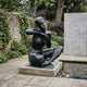 Life-Size Contemporary Seated Nude Female Figure Bronze Sculpture by Giant Sculptures with black patina, displayed on a plinth beside a pebble-lined garden pond.