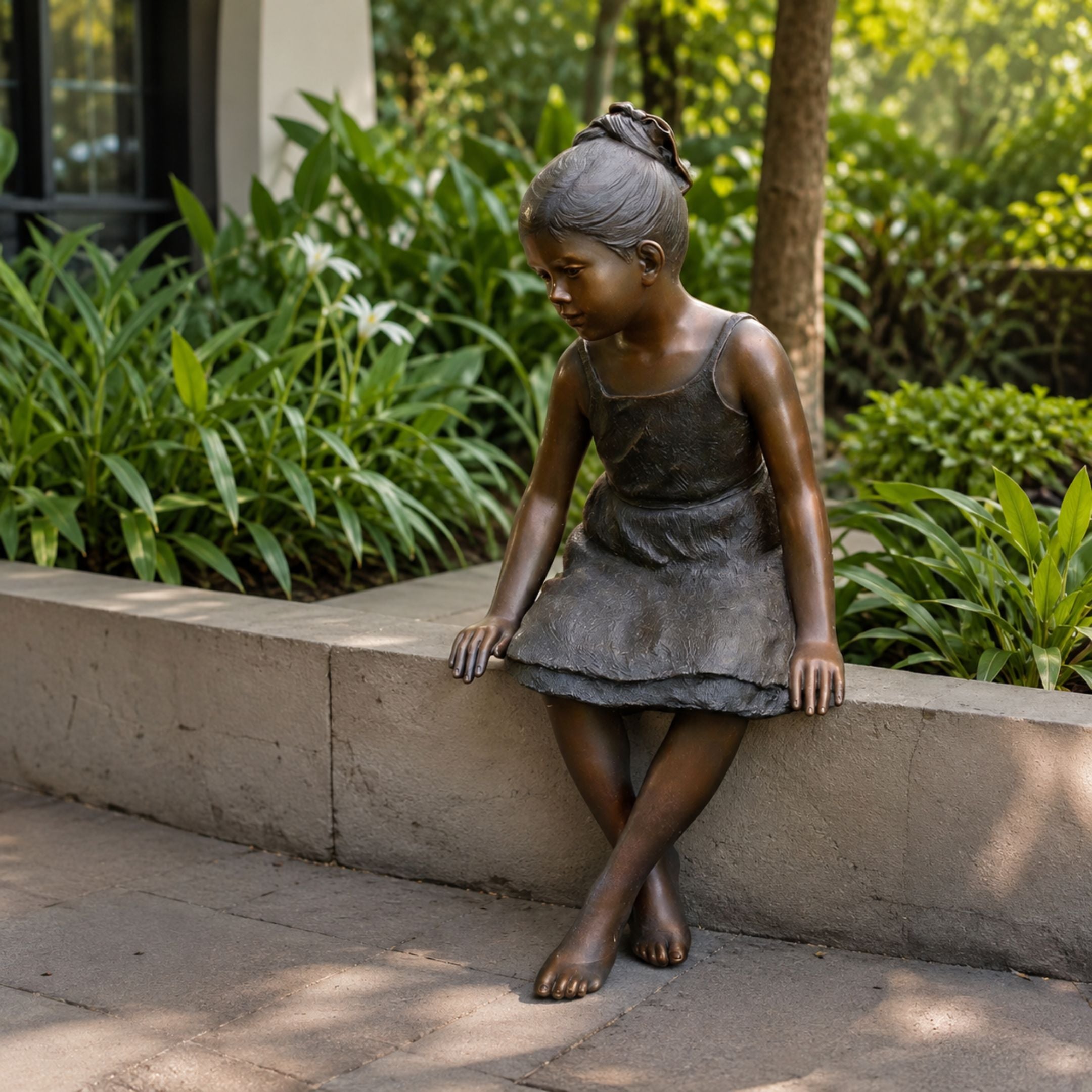 Life-Size Contemporary Sitting Girl Bronze Sculpture, 130cm, seated on a stone ledge with legs crossed, set outdoors amid green garden foliage.