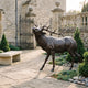 Life-Size Traditional Bugling Elk Bronze Sculpture by Giant Sculptures displayed on a flagstone courtyard beside a stone bench and iron gate of a historic estate.