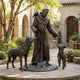 Life-Size Traditional Robed Saint with Wolf and Animal Companions Bronze Sculpture by Giant Sculptures, shown in a stone courtyard with wolf, lamb, and birds.