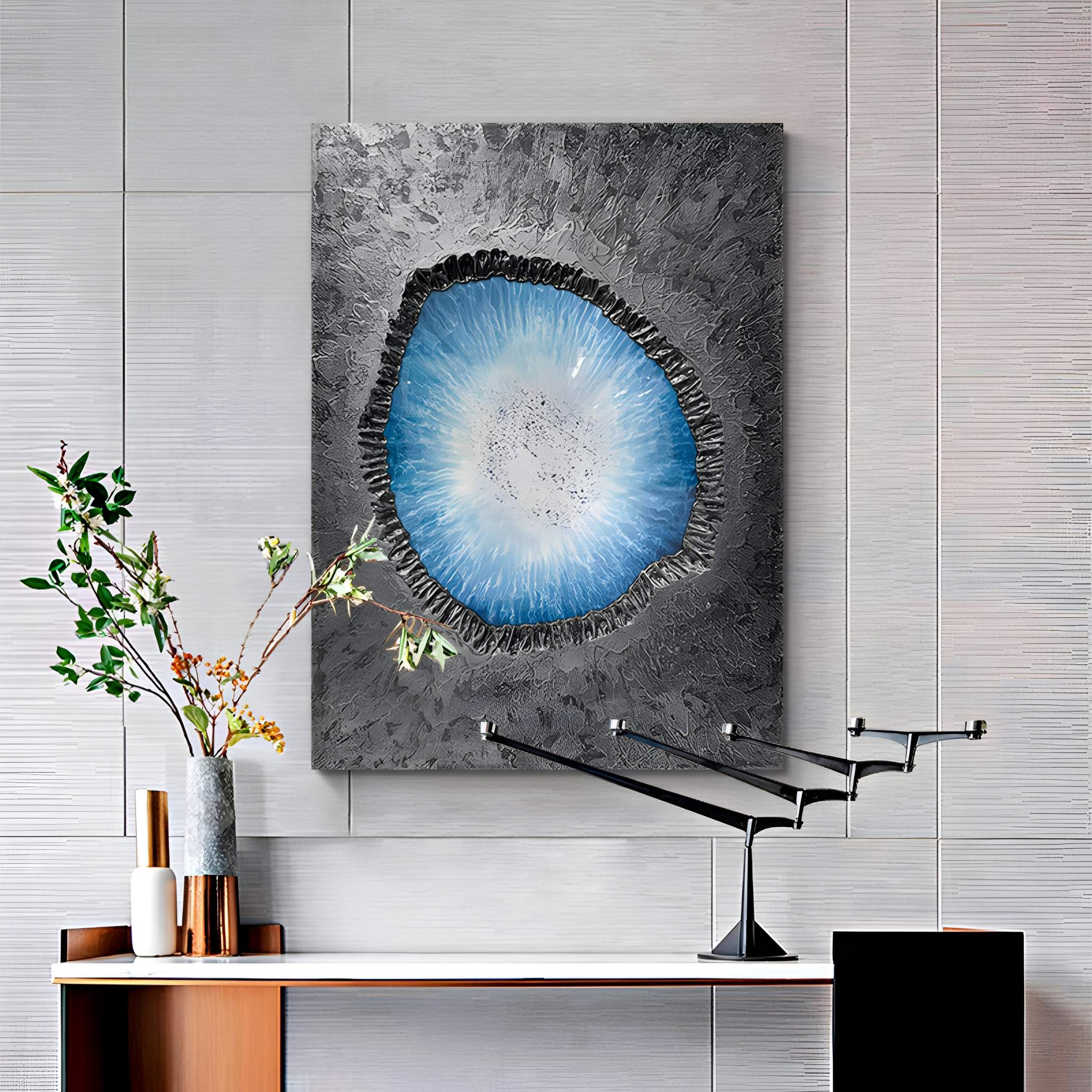 A modern interior features the Vorthera Sky Radiance Textured Silver 3D Wall Art by Giant Sculptures as contemporary decor. Nearby, a small table with vases, lush foliage, a black angular desk lamp, and textured gray wall panels complete the look.